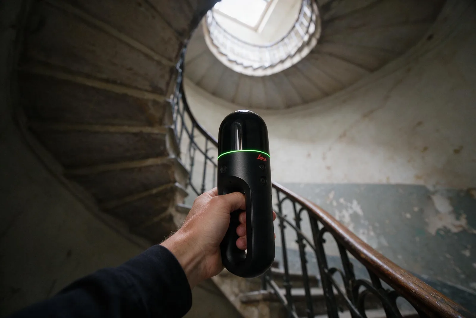 Scanner laser 3D mobile tenu a la main dans un escalier de service en colimacon, marches en pierre et balustrade en ferronnerie.